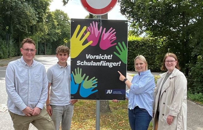 Vorsicht Schulanfänger: Gruppe posiert vor Warnschild mit Handabdrucken.