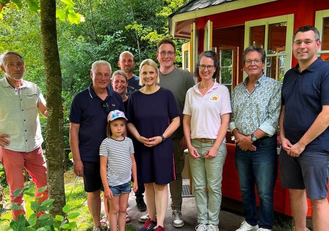 Gruppe von Menschen vor rotem Gartenhäuschen im Grünen, fröhlich posierend.