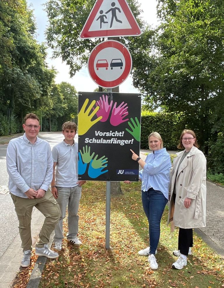 Vorsicht Schulanfänger: Gruppe posiert vor Warnschild mit Handabdrucken.